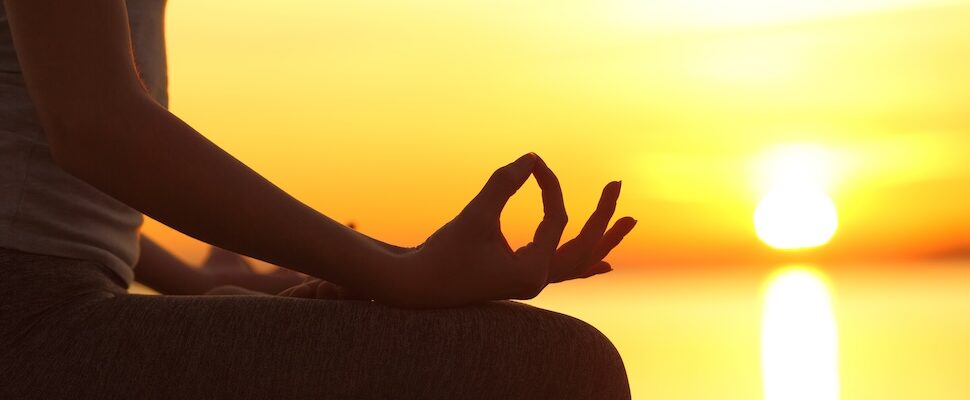 Woman seated with mudra at sun rise for setting intentions that work