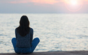 Pensive woman seated at the water for when to see a spiritual life coach